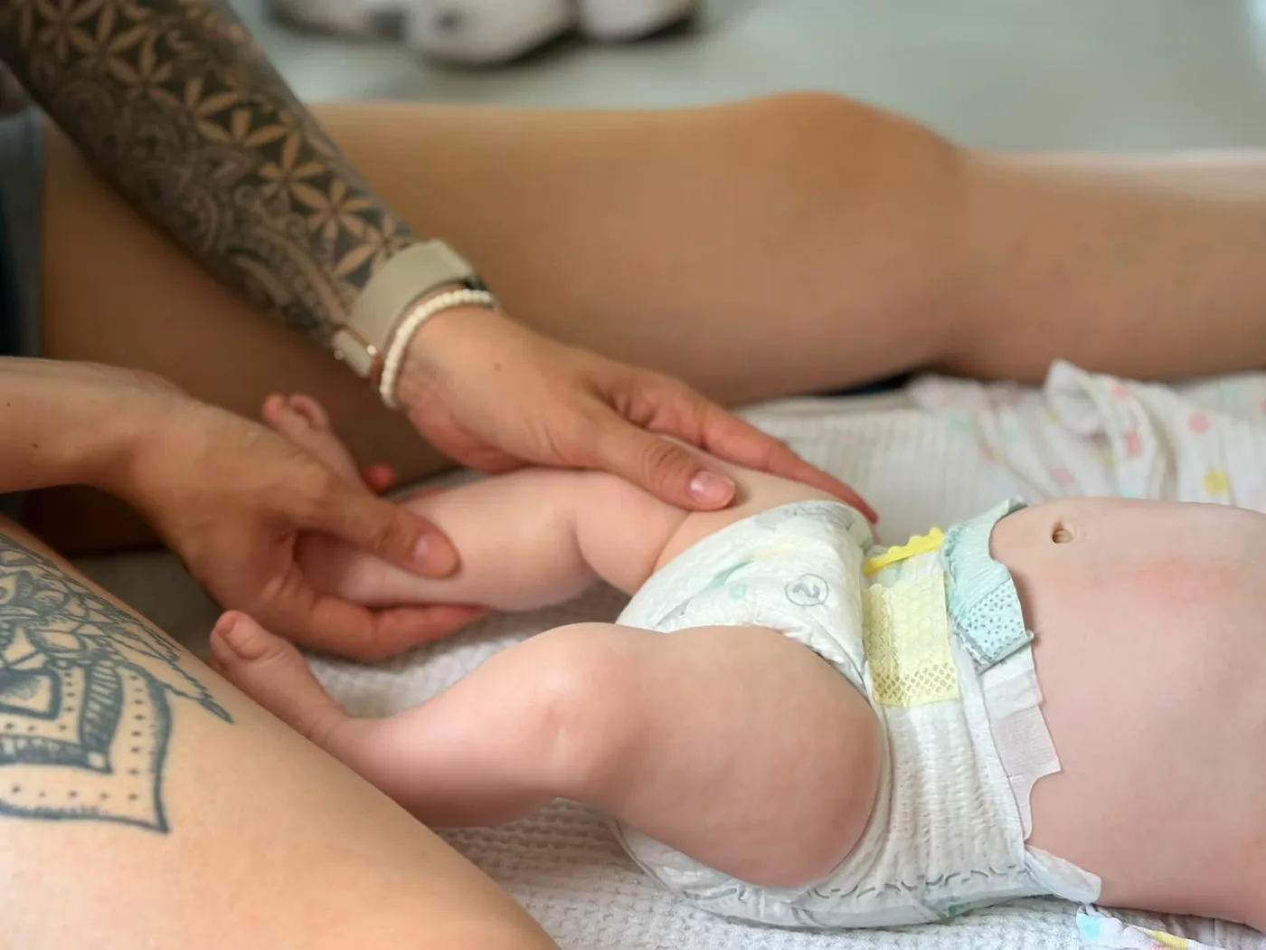 Hebamme massiert sanft das Bein eines Babys in der Babymassage